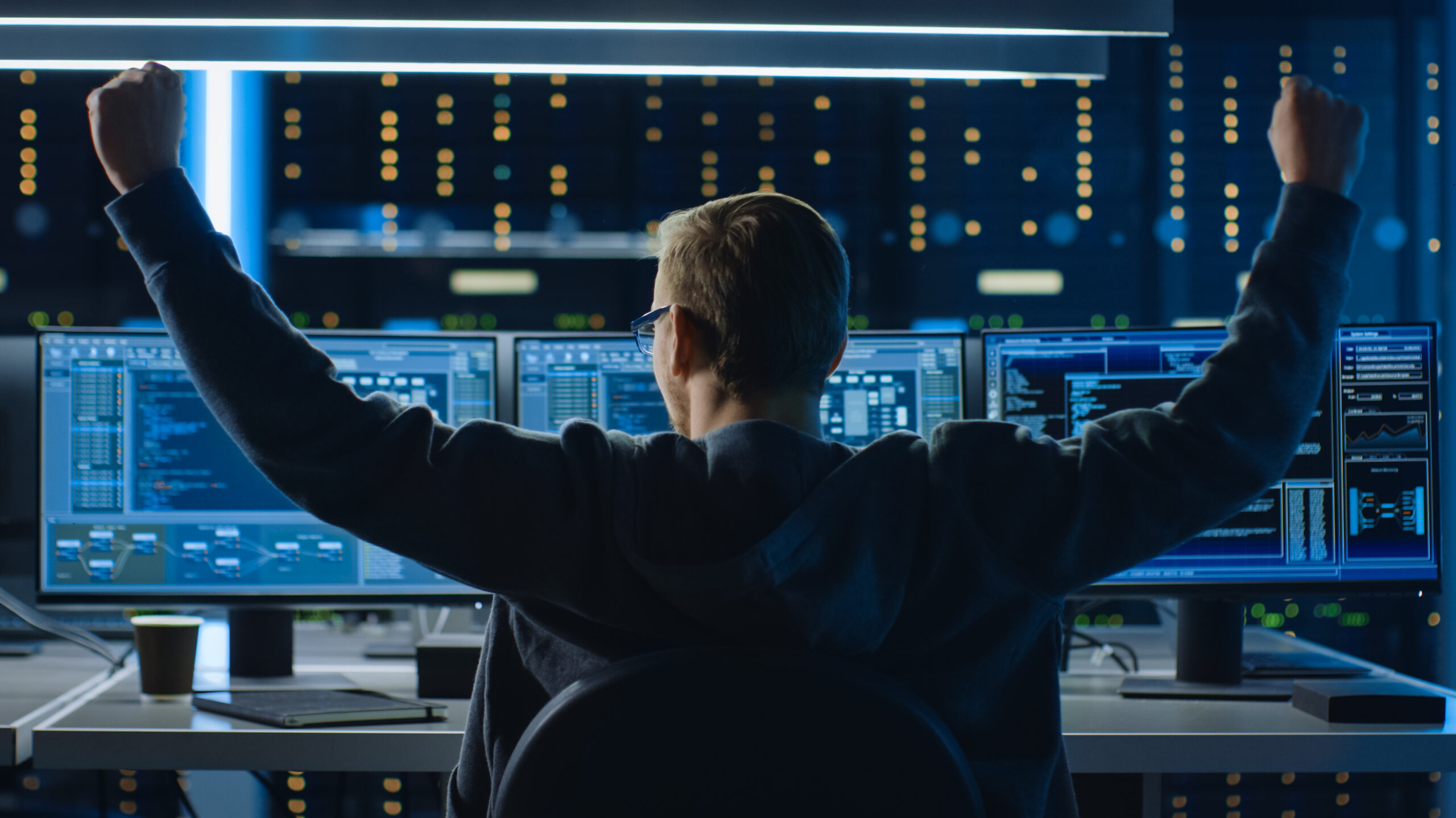 IT Specialist Working on Personal Computer with Monitors Showing Coding Language Program, He Celebrates His Success by Doing YES Gesture. Technical Room of Data Center.